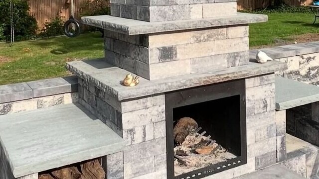 Custom-built stone outdoor fireplace featuring integrated wood storage and bench seating, expertly crafted by Constructive Greens